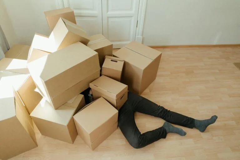 A person overwhelmed by cardboard boxes during a home move, symbolizing stress and relocation.